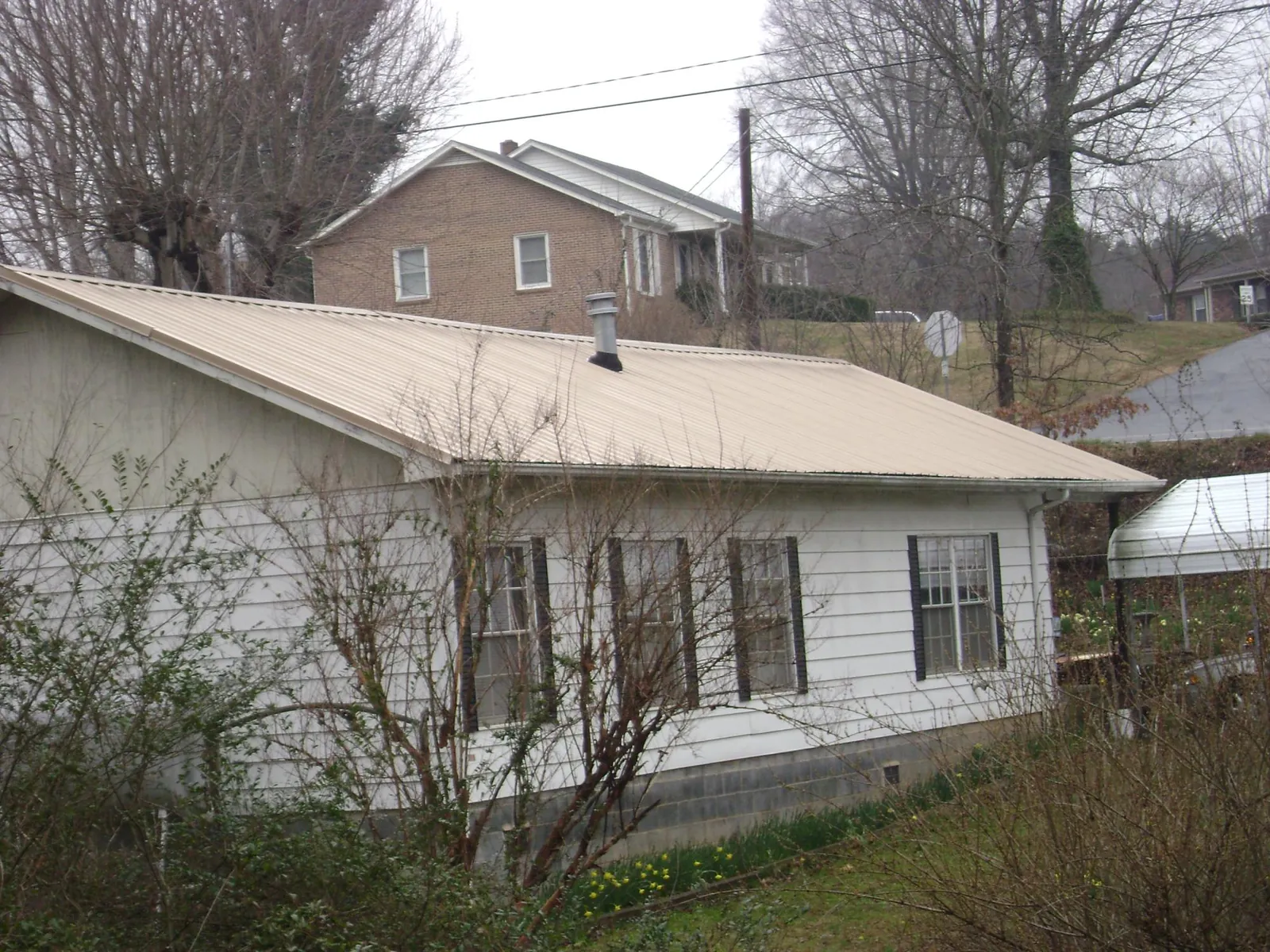 Tan metal roof on a white sided house set into a hillside — Commercial Roofing by Roofing Brothers in Chandler